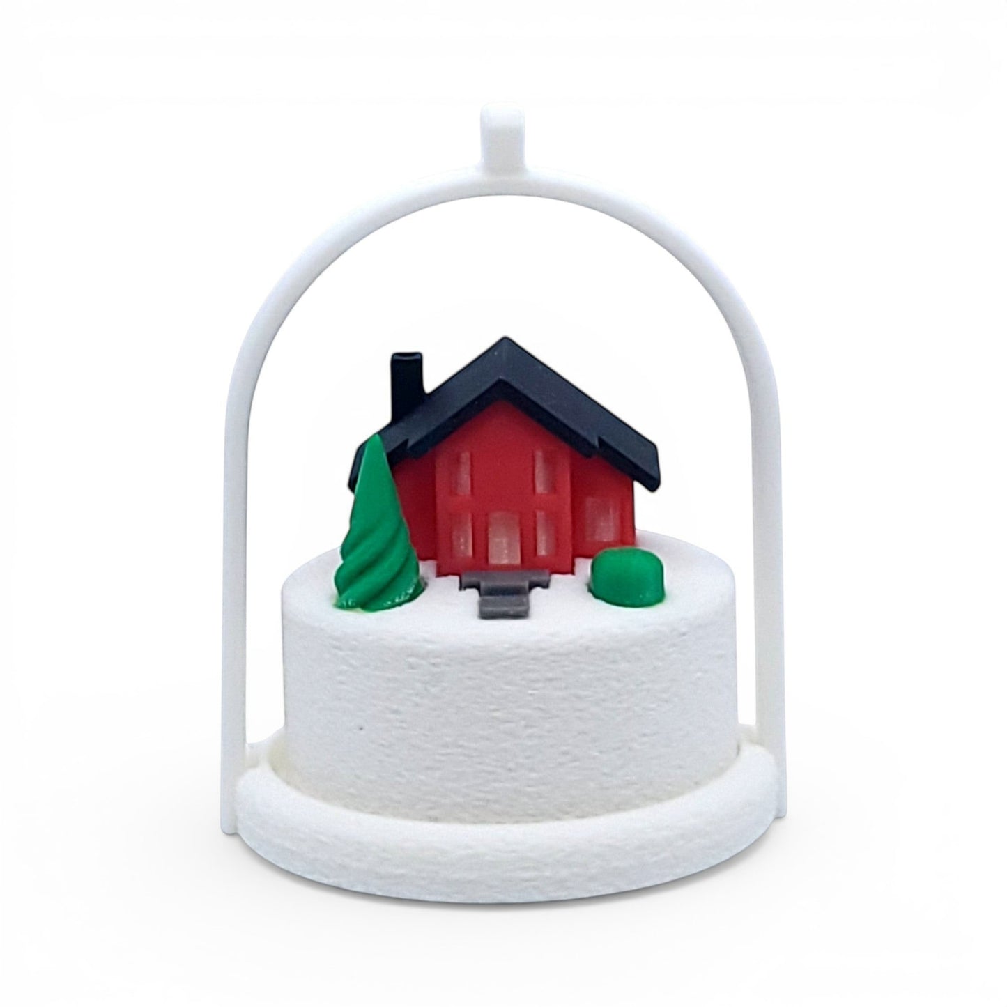 Miniature winter village ornament with a red house, green tree, and white arched frame. Front view of red house, in tree stand with light off.