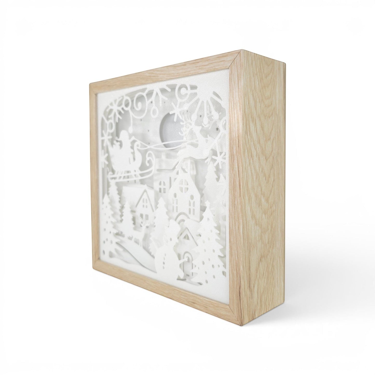 Christmas light box with a layered paper scene of Santa in his sleigh over a snowy village. Front right corner.