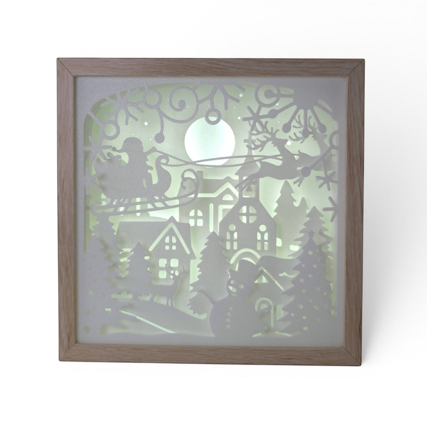 Christmas light box with a layered paper scene of Santa in his sleigh, reindeer, snowman, and village under a full moon. Illuminated box front shot.