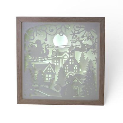 Christmas light box with a layered paper scene of Santa in his sleigh, reindeer, snowman, and village under a full moon. Illuminated box front shot.