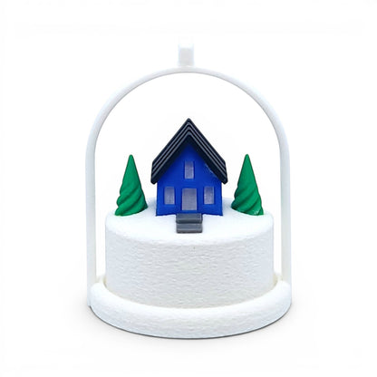 Miniature blue house ornament with green trees on a snowy base inside a white arched frame. Front view of blue house, in tree stand with light off.