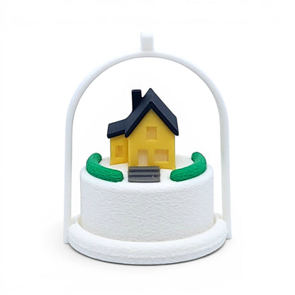 Miniature yellow house ornament with a black roof inside a white arched frame for holiday decor. Front view of yellow house, in tree stand with light off.