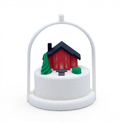Miniature winter village ornament with a red house, green tree, and white arched frame. Front view of red house, in tree stand with light off.