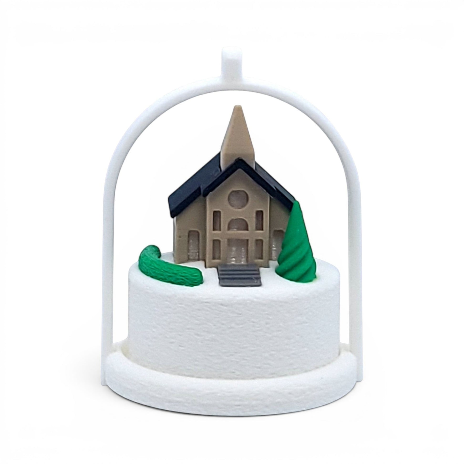 Miniature winter village church ornament with a white arched frame and snowy base. Front view of brown church, in tree stand with light off.
