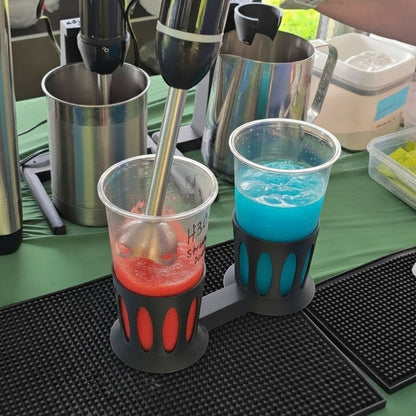 Black PLA plastic dual cup holder stabilizing two clear cups while using an immersion blender