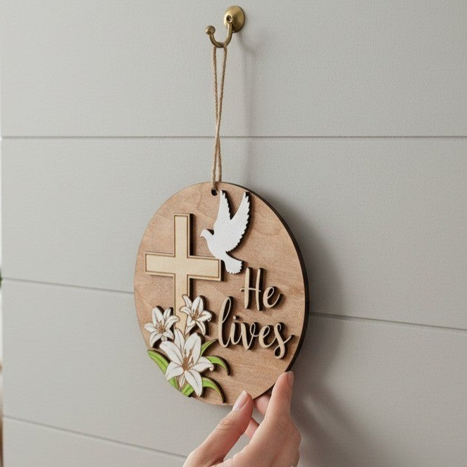 He Lives Easter wooden ornament with cross, lilies, and dove. Natural wood finish.