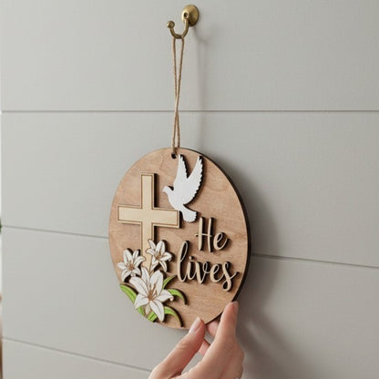 He Lives Easter wooden ornament with cross, lilies, and dove. Natural wood finish.