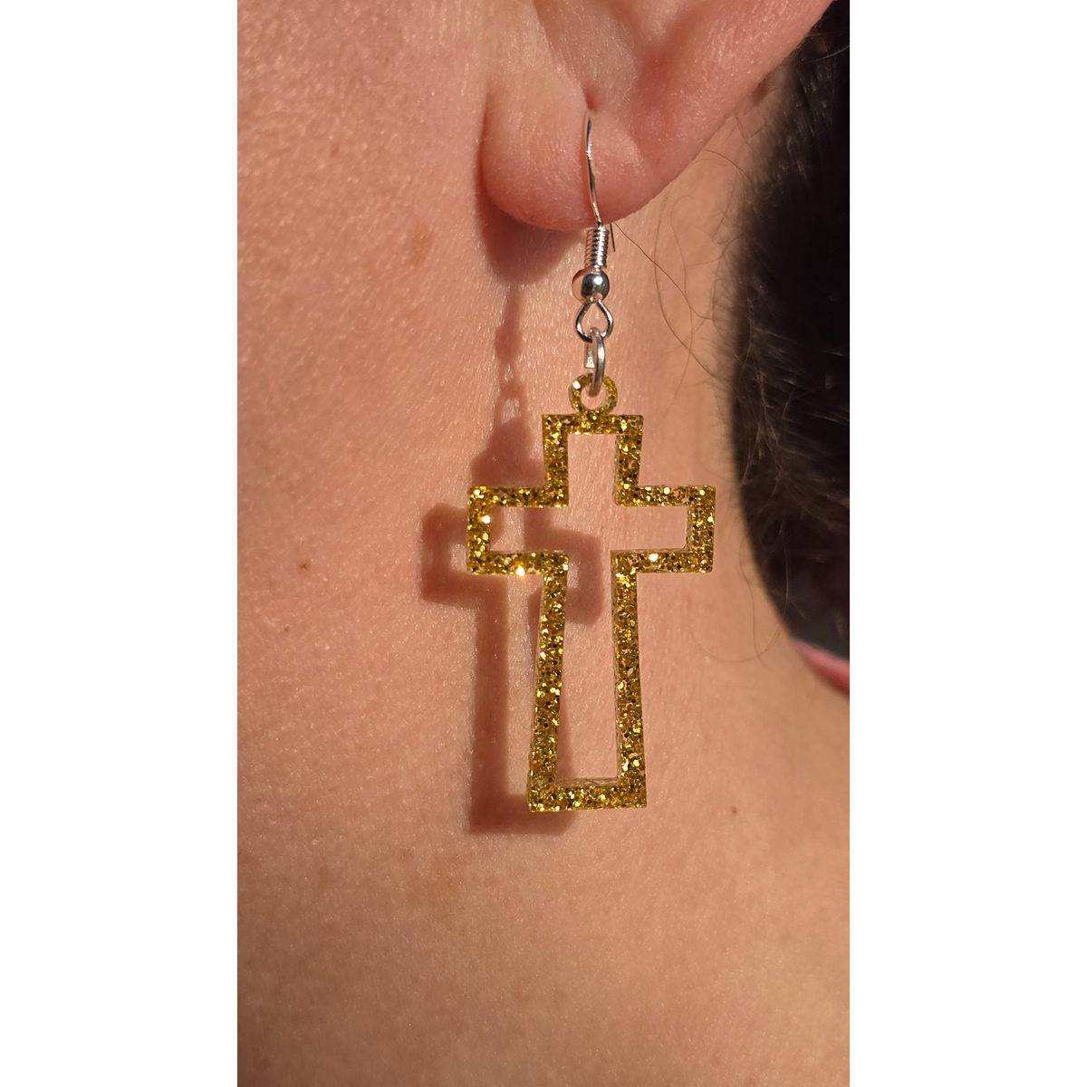 gold glitter acrylic open-frame cross dangle earrings with hypoallergenic hooks worn on ear