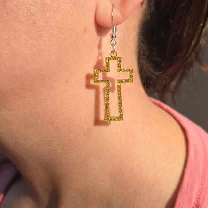 gold glitter open-frame cross dangle earrings with hypoallergenic hooks worn on a female earlobe