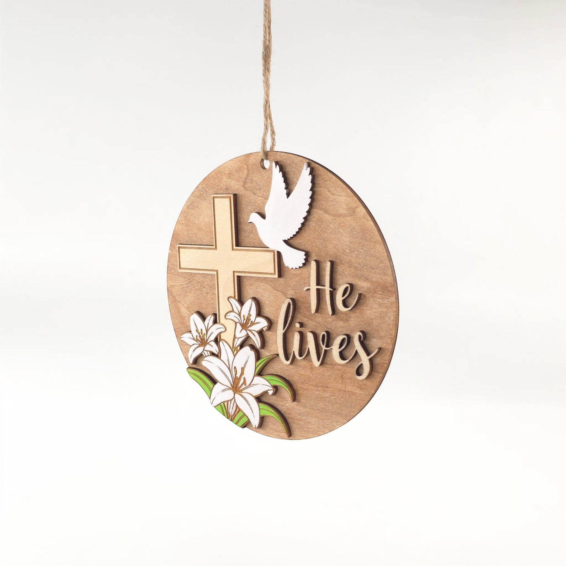 He Lives Easter wooden ornament with cross, lilies, and dove. Natural wood finish.
