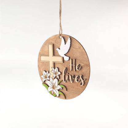 He Lives Easter wooden ornament with cross, lilies, and dove. Natural wood finish.