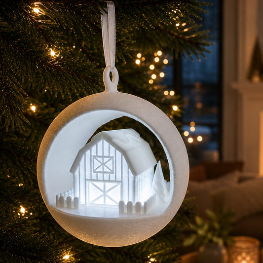 illuminated white barn ornament with picket fence and trees, hanging on a Christmas tree. Light on, front right corner of ornament.
