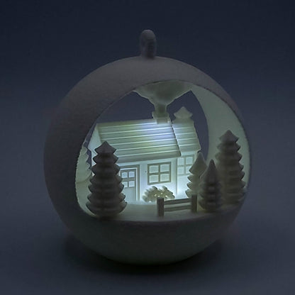 Illuminated Winter Farmhouse Ornament, a miniature farmhouse with trees and fence, made of PLA plastic. Light on, dim background, front of ornament.