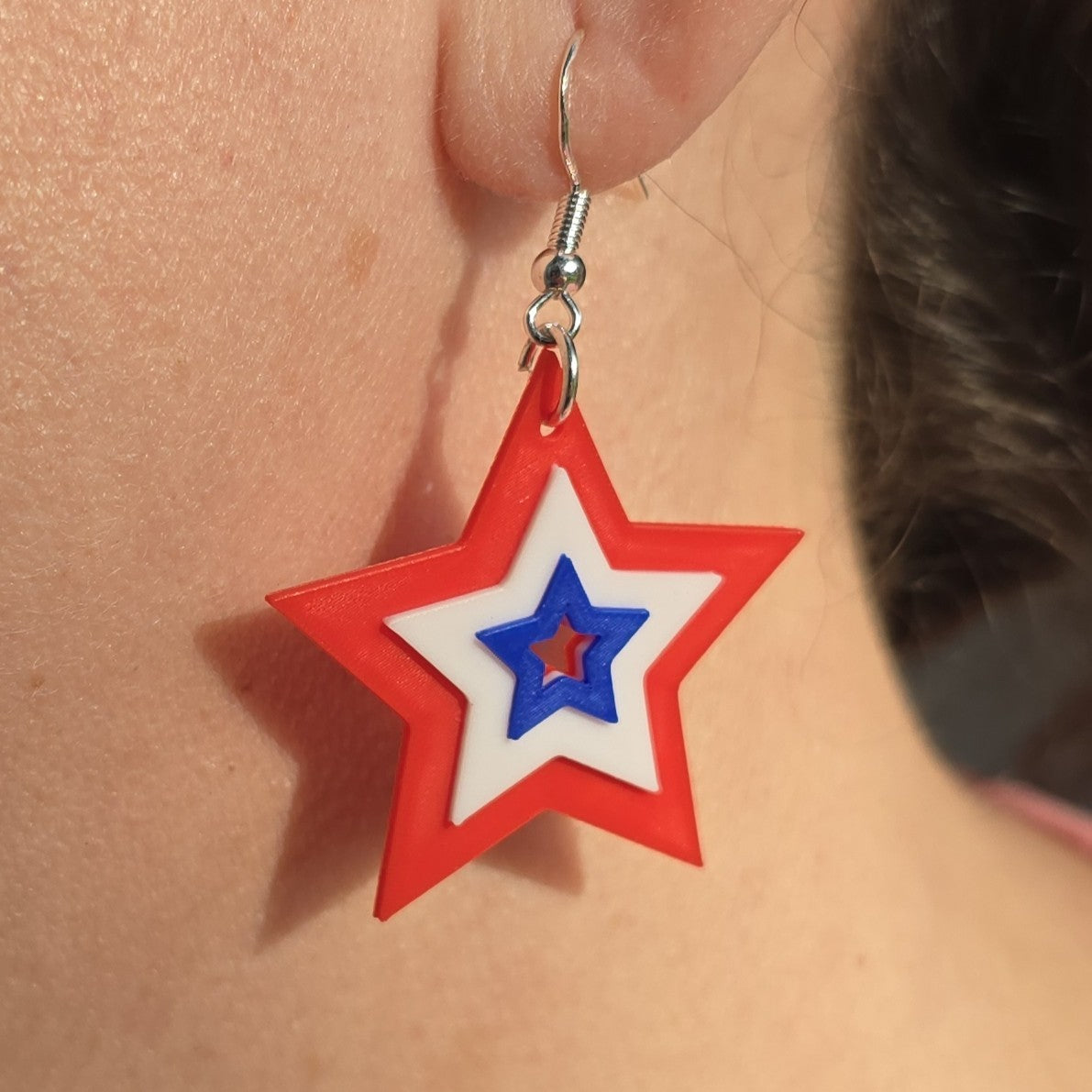 layered star dangle earrings in red, white, and blue worn on an earlobe