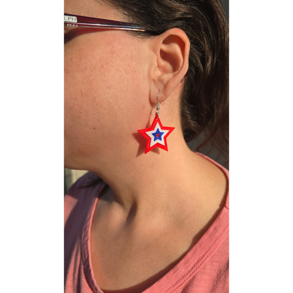 layered star dangle earrings in red, white, and blue worn by a woman in a pink shirt.