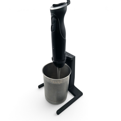 black immersion blender stand holding a blender and metal mixing cup on a white background