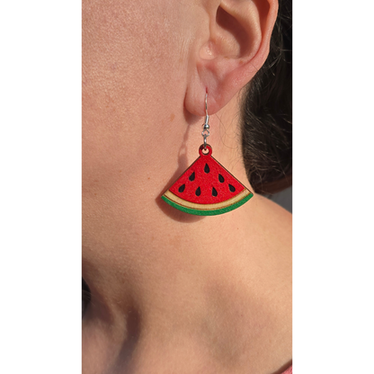 watermelon dangle earrings made of hand-painted basswood with hypoallergenic silver hooks hanging from ear for scale.