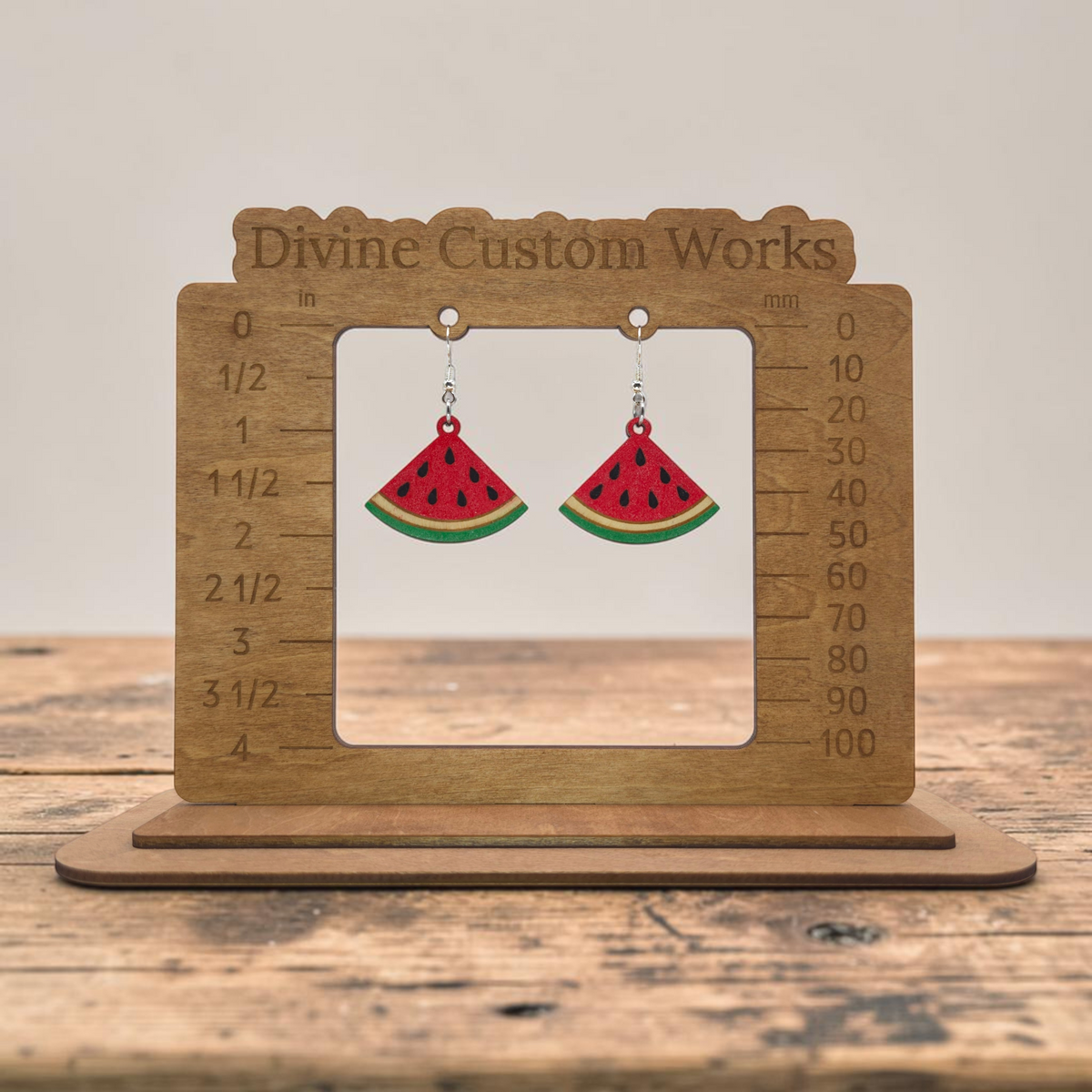watermelon dangle earrings made of hand-painted basswood with hypoallergenic silver-plated hooks hanging from sizing board.